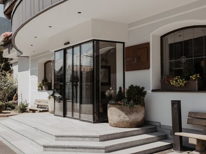 Kurzurlaub in Tirol? Ja, bitte! Eingang mit Glasfront und Treppenstufen zu einem Café mit Blumen und Bänken