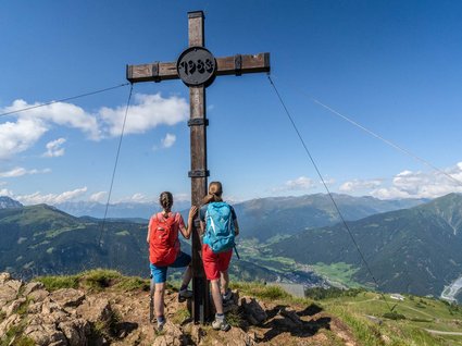 Wanderhotel in Tirol: herrliche Berge und Täler Zwei Wanderer stehen am Gipfelkreuz mit Bergpanorama im Hintergrund
