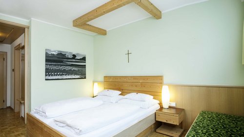 Benvenuti al nostro hotel a Matrei Camera da letto verde chiaro con letto in legno, quadro e croce al muro