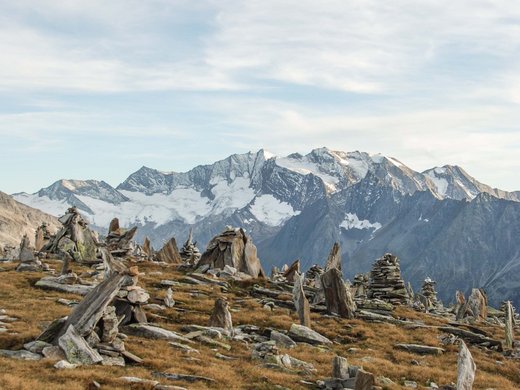 Welches Skigebiet bei Matrei am Brenner magst du am liebsten? Steinmännchen auf Almwiese vor schneebedeckten Bergen unter bewölktem Himmel