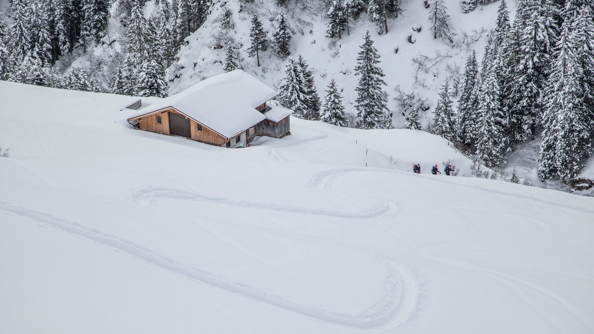 Sporthotel in Tirol: Aktivurlaub im Parkhotel Matrei Schneebedeckte Hütte am Hang mit Skispuren und Wanderern im Winterwald