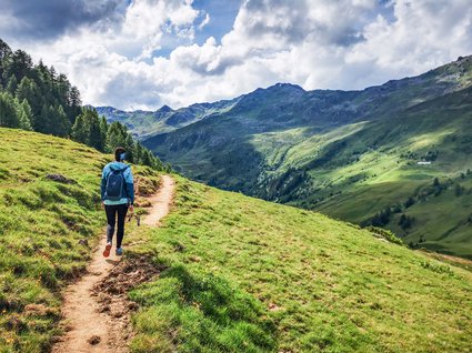 Wanderhotel in Tirol: herrliche Berge und Täler Wanderer auf einem Pfad in grünen Bergen unter bewölktem Himmel
