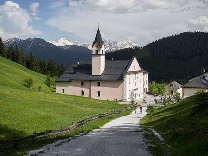 By car to Italy: stopover in Wipptal Path with cyclists heading to a church in the mountains during summer