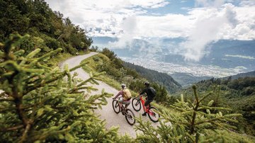 News (Liste) Zwei Radfahrer auf einem Bergweg mit Blick auf Tal und Wolken