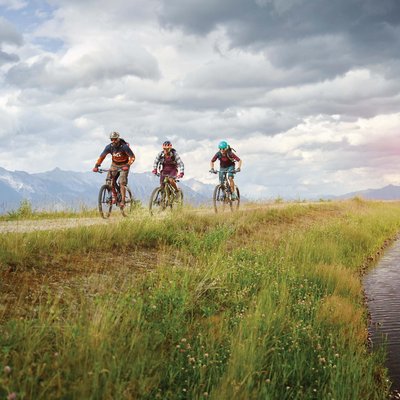 News (Liste) Drei Mountainbiker fahren auf einem Weg neben einem Gewässer in den Bergen