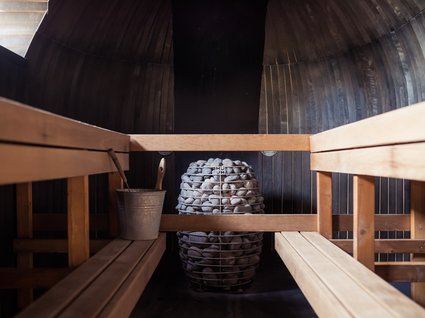 Kurzurlaub in Tirol? Ja, bitte! Innenraum einer Sauna mit Holzliegen und Saunaofen mit Steinen