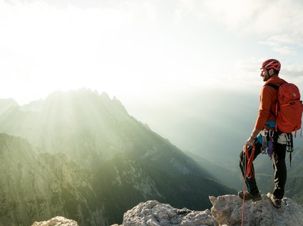 Holidays at the Brenner Pass: hiking and climbing Climber with red backpack overlooks sunlit mountain peaks