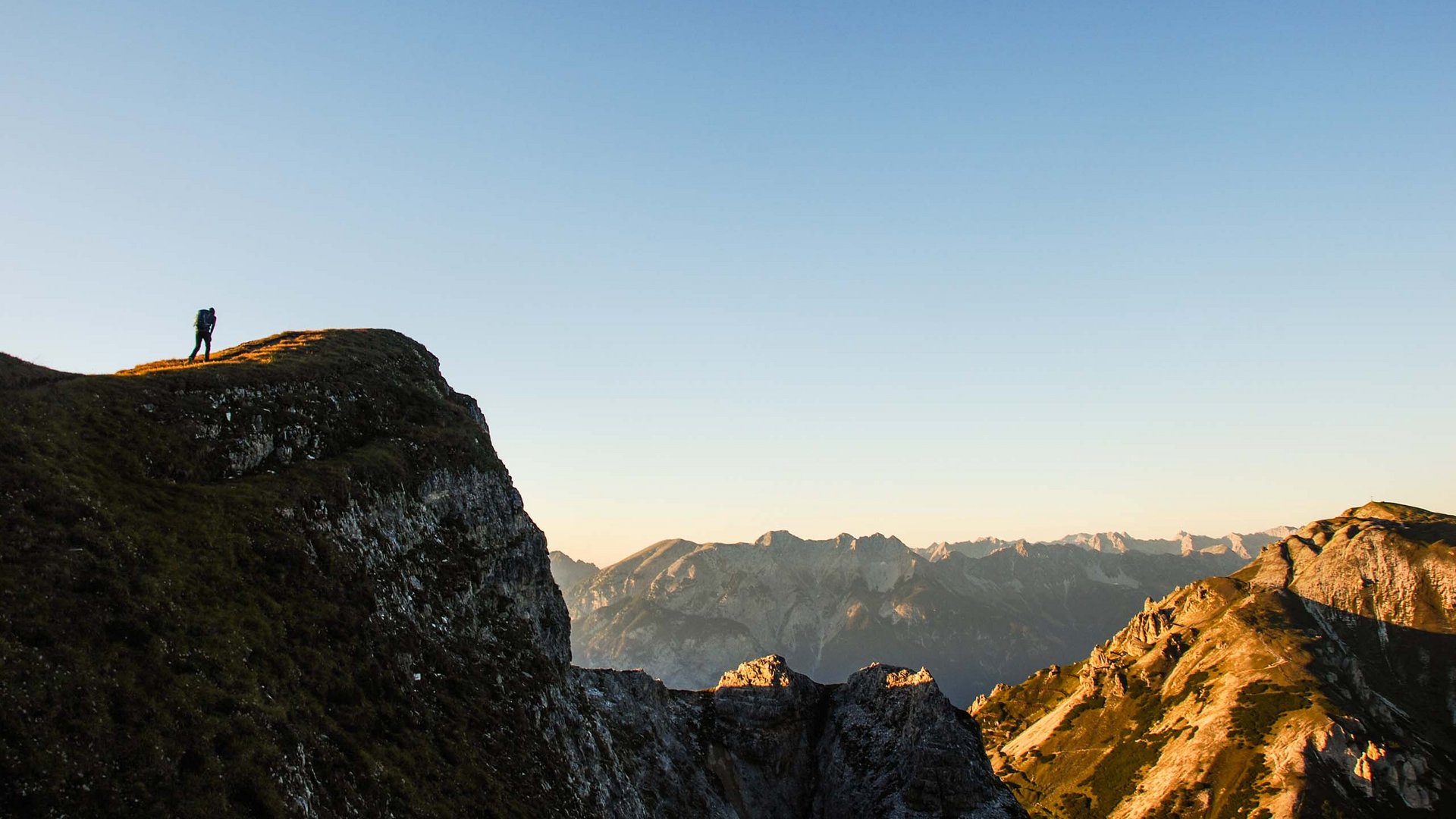 Hiking in Matrei am Brenner Hiker on mountain ridge at sunset with mountainous landscape in background