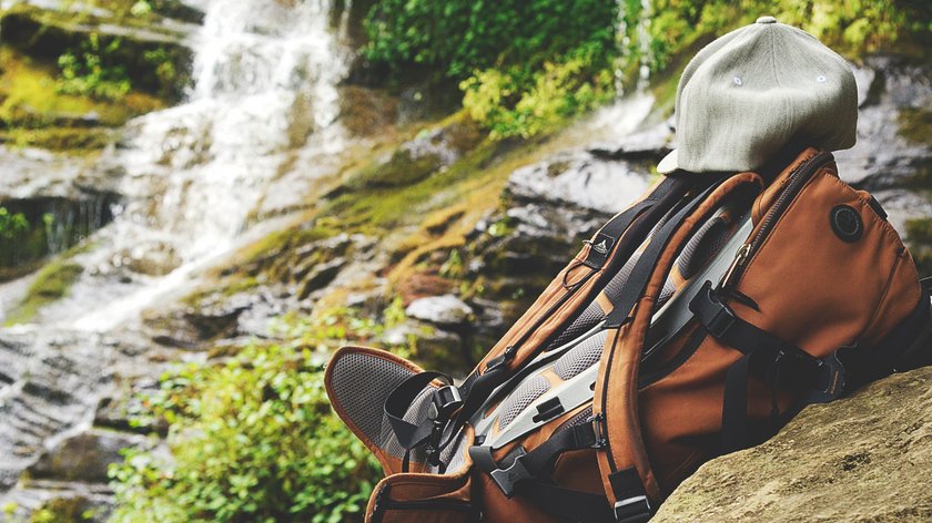 Wandertipp: der WildeWasserWeg Rucksack mit grauer Mütze vor Wasserfall und Felsen