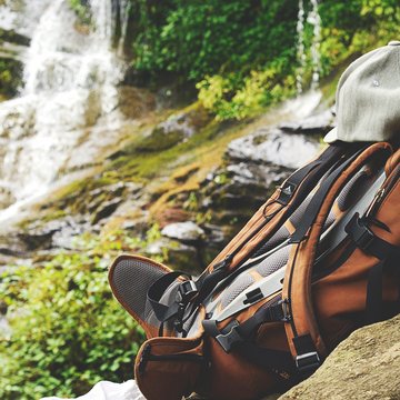 Neuigkeiten aus dem Motorradhotel in Tirol Rucksack mit grauer Mütze vor Wasserfall und Felsen