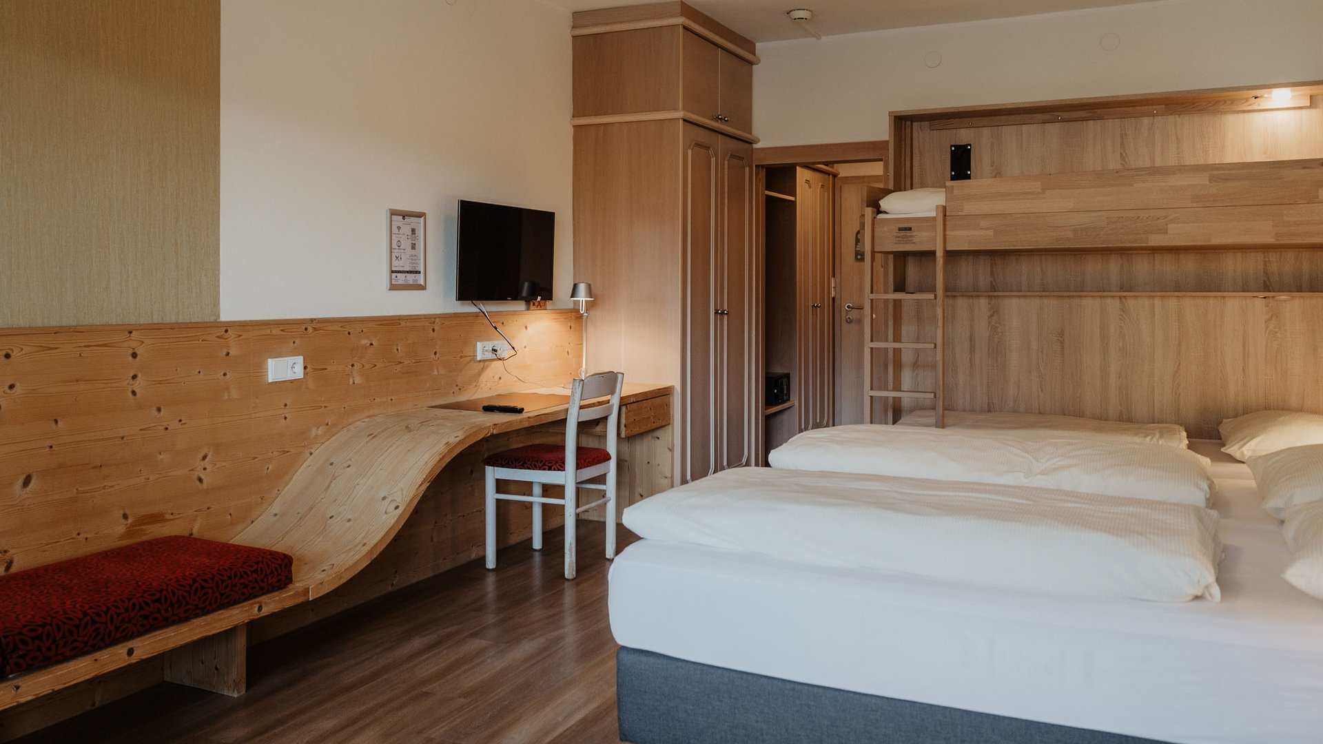 Camera d'albergo luminosa con letto matrimoniale e a castello in legno