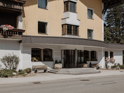 Kurzurlaub in Tirol? Ja, bitte! Außeneingang eines Gebäudes mit Bänken und Blumendekoration