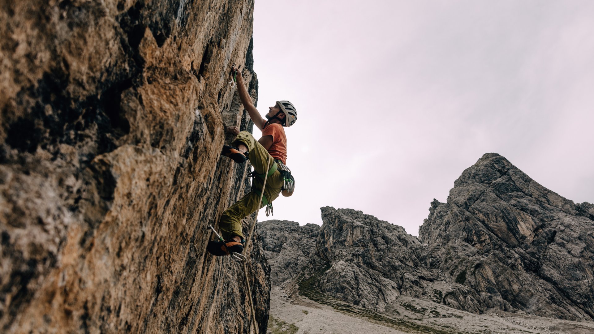 Kletterer mit Helm erklimmt steile Felswand in bergiger Landschaft