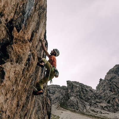 News (Liste) Kletterer mit Helm erklimmt steile Felswand in bergiger Landschaft