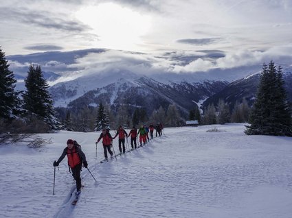 Die schönsten Skitouren in Tirol Gruppe beim Skitourengehen auf schneebedecktem Bergweg mit bewölktem Himmel