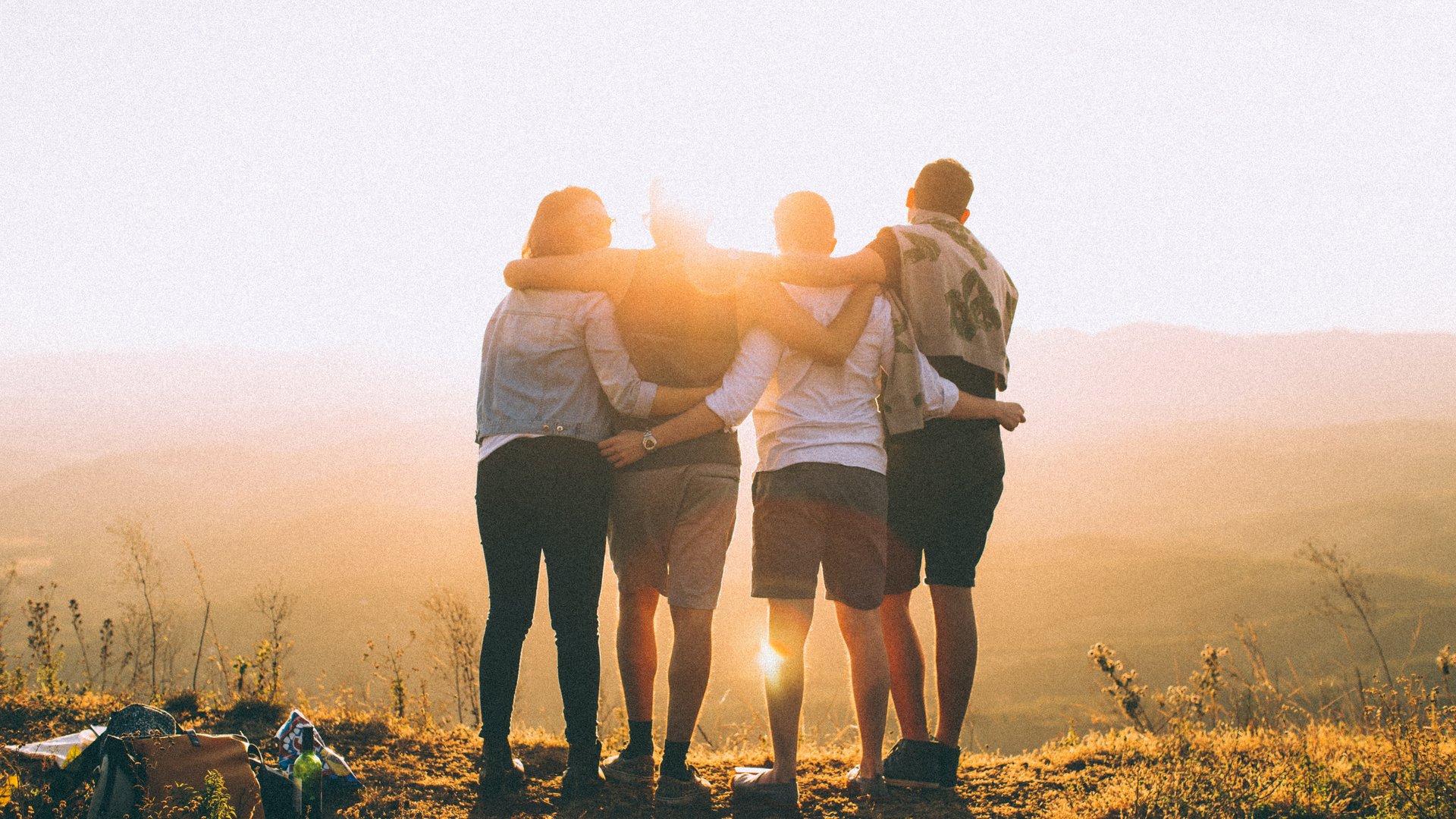 Four friends hugging and watching the sunset on a hilltop