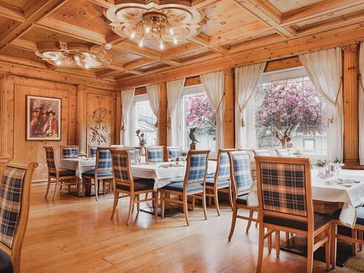 Deliciousness awaits in our restaurant in Matrei am Brenner Cozy dining area with wooden furniture and large windows overlooking blooming trees
