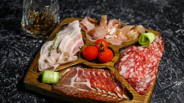 News (Liste) Holzbrett mit verschiedenen Wurstsorten, Tomaten und Gurke, Glas mit Getränk daneben