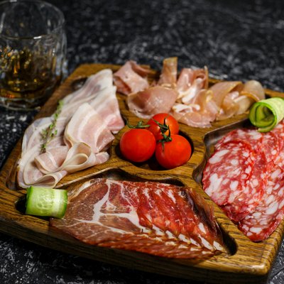 News (Liste) Holzbrett mit verschiedenen Wurstsorten, Tomaten und Gurke, Glas mit Getränk daneben