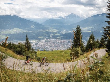 Parkhotel Matrei: Mountainbikehotel in Tirol Zwei Mountainbiker auf Bergweg mit Blick auf Stadt und Berge im Hintergrund