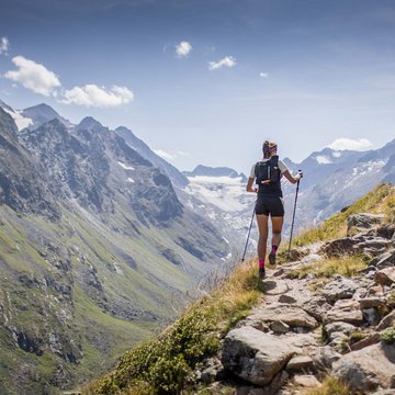 Neuigkeiten aus dem Motorradhotel in Tirol Frau wandert mit Stöcken auf einem Bergpfad in Alpenlandschaft