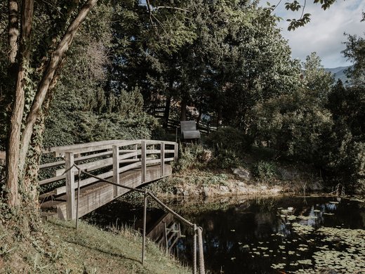 Herzlich willkommen in unserem Hotel in Matrei am Brenner Holzbrücke über einen Teich umgeben von Bäumen und Pflanzen