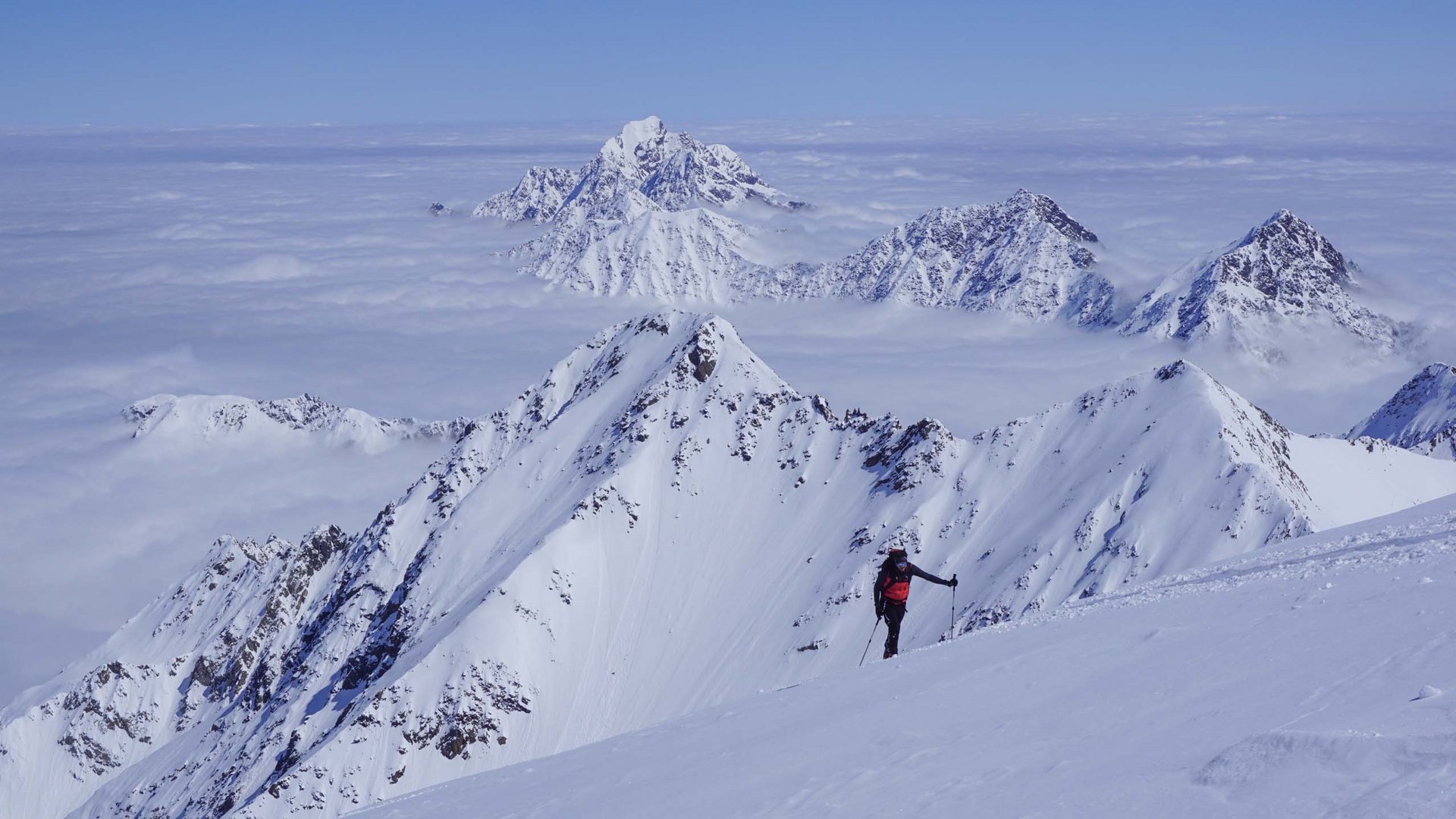 Alpinista con zaino rosso in neve sulle cime delle Alpi sopra le nuvole