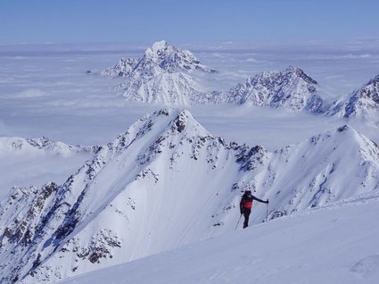 Die schönsten Skitouren in Tirol Bergsteiger im roten Rucksack wandert durch verschneite Alpen mit Wolkenschicht darunter