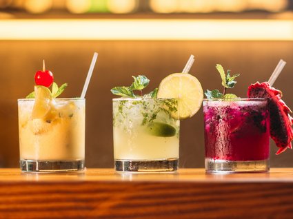 Bar per il vostro giro in moto in Austria? Tre cocktail colorati con frutta e cannucce su bancone di legno