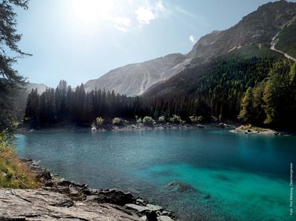 Ausflugstipps aus unserem Hotel: Innsbruck und Umgebung Klarer Bergsee mit Tannenwald und Bergen bei sonnigem Himmel