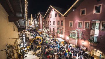 News (Teaser) Belebte Straße mit geschmückten Häusern und Menschen bei Nacht