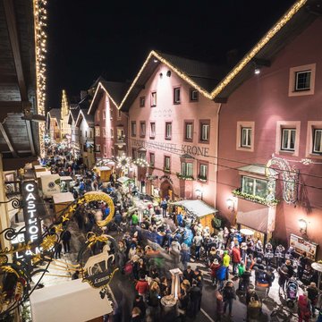 News (Teaser) Belebte Straße mit geschmückten Häusern und Menschen bei Nacht
