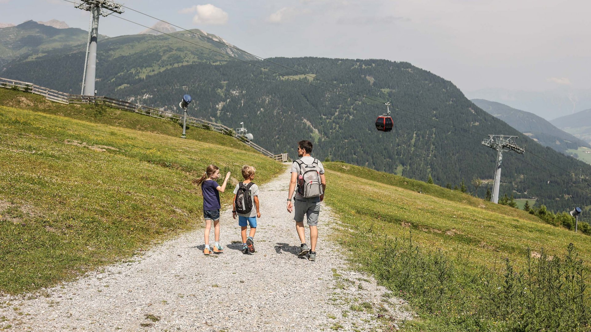 Wanderhotel in Tirol: herrliche Berge und Täler Vater wandert mit zwei Kindern auf Bergweg unter Seilbahn in den Alpen