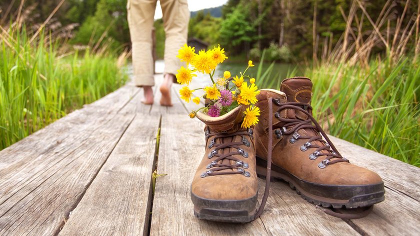 Frühlingswanderung durchs Wipptal Wanderschuhe mit Blumen auf Holzsteg, Person barfuß im Hintergrund