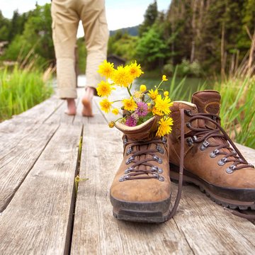 Neuigkeiten aus dem Motorradhotel in Tirol Wanderschuhe mit Blumen auf Holzsteg, Person barfuß im Hintergrund