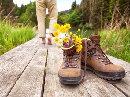 Ausflugstipps aus unserem Hotel: Innsbruck und Umgebung Wanderschuhe mit Blumen auf Holzsteg, Person barfuß im Hintergrund
