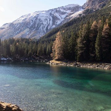 Neuigkeiten aus dem Motorradhotel in Tirol Klarer Bergsee mit Nadelwald und schneebedeckten Bergen im Hintergrund