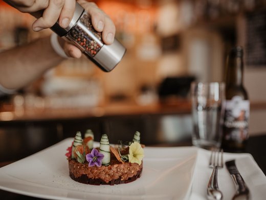 Hotel in Tirol mit Halbpension gesucht? Frau würzt ein kunstvoll angerichtetes Gericht mit Pfeffer