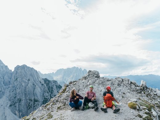 Wanderhotel in Tirol: herrliche Berge und Täler Drei Kletterer machen Pause auf einem felsigen Berggipfel mit Bergpanorama