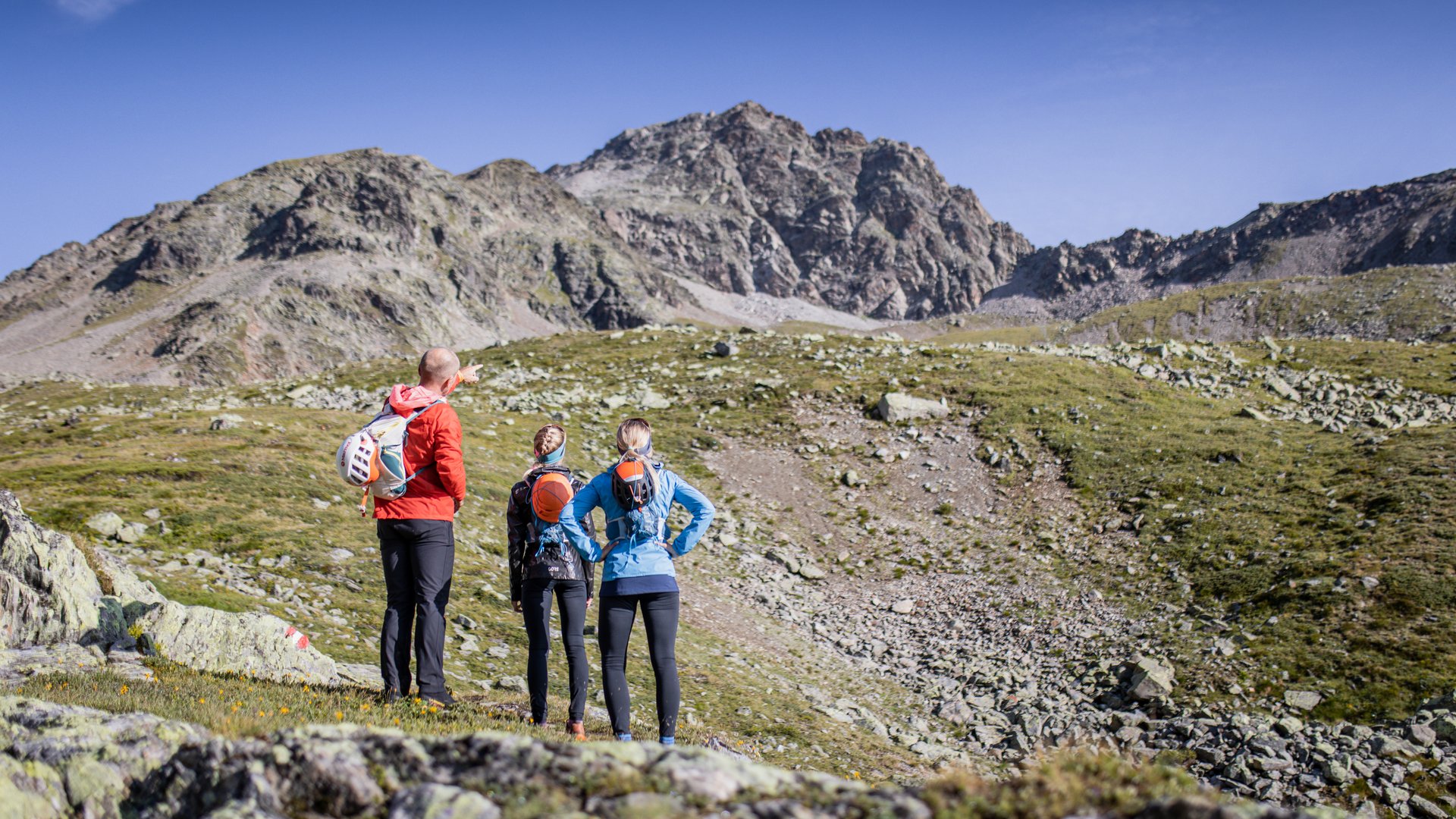 Three hikers looking at rocky mountain landscape under clear sky