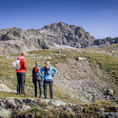 News (Liste) Drei Wanderer schauen auf felsige Berglandschaft unter klarem Himmel