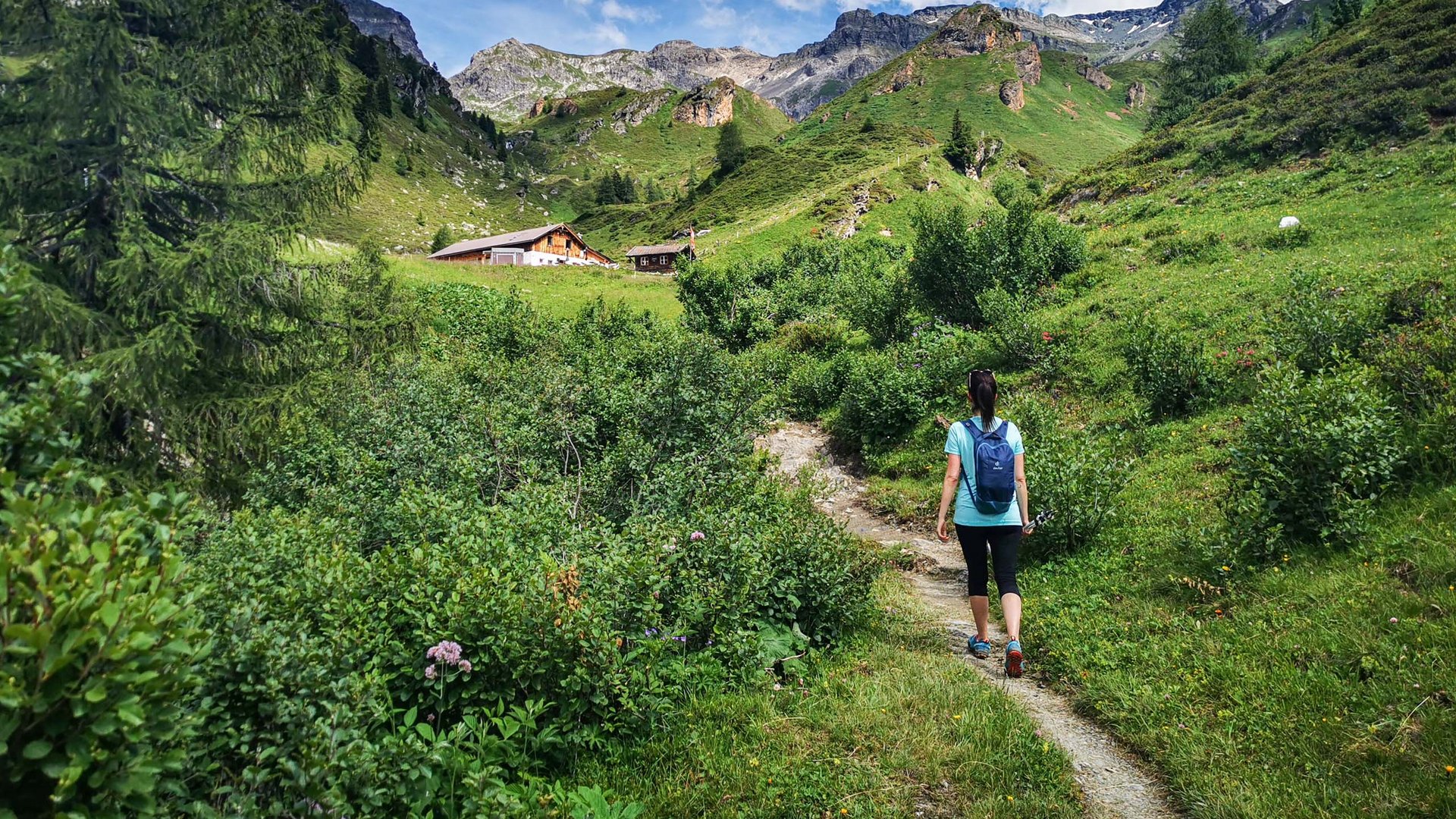 Wanderhotel in Tirol: herrliche Berge und Täler Wandererin auf einem Pfad in den grünen Bergen bei blauem Himmel