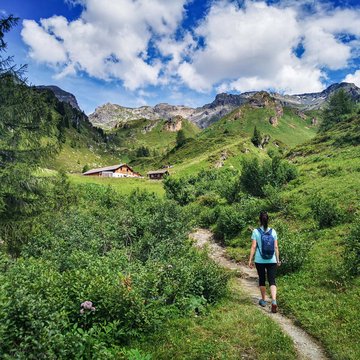 Neuigkeiten aus dem Motorradhotel in Tirol Wandererin auf einem Pfad in den grünen Bergen bei blauem Himmel