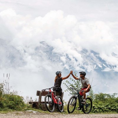 News (Liste) Zwei Radfahrer in Berglandschaft geben sich High Five