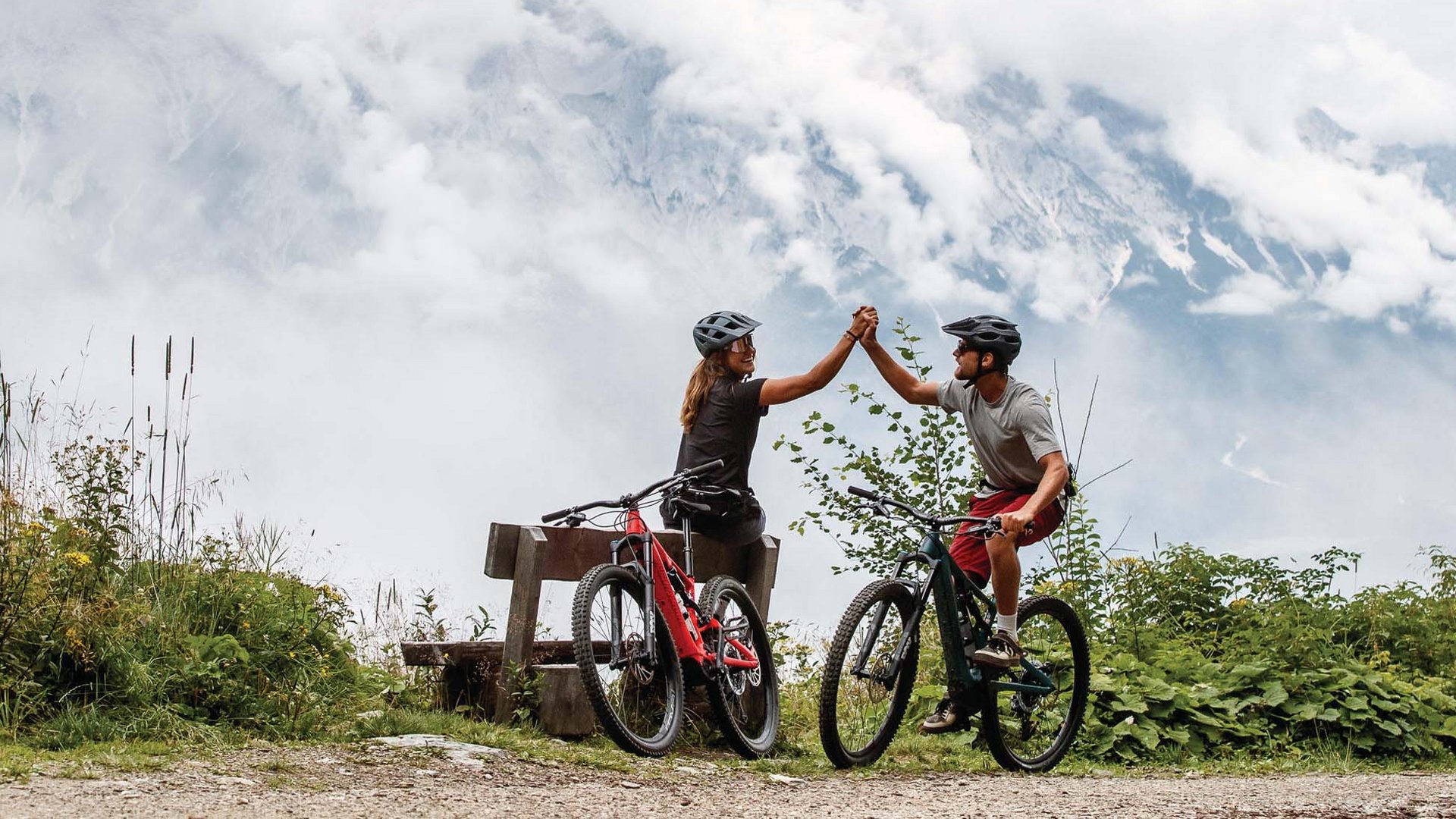 Two cyclists high five with mountain scenery in the background
