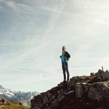 Neuigkeiten aus dem Motorradhotel in Tirol Mann mit Rucksack steht auf felsigem Berggipfel mit schneebedeckten Bergen im Hintergrund