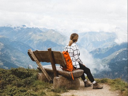 Wanderhotel in Tirol: herrliche Berge und Täler Frau mit rotem Rucksack sitzt auf Bank und schaut auf Berglandschaft