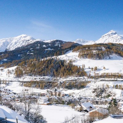 News (Liste) Schneebedeckte Alpenlandschaft mit Dorf und Bergen unter blauem Himmel