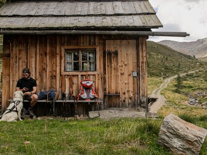 Wanderhotel in Tirol: herrliche Berge und Täler Wanderer mit Hund vor einer Holzhütte in den Bergen