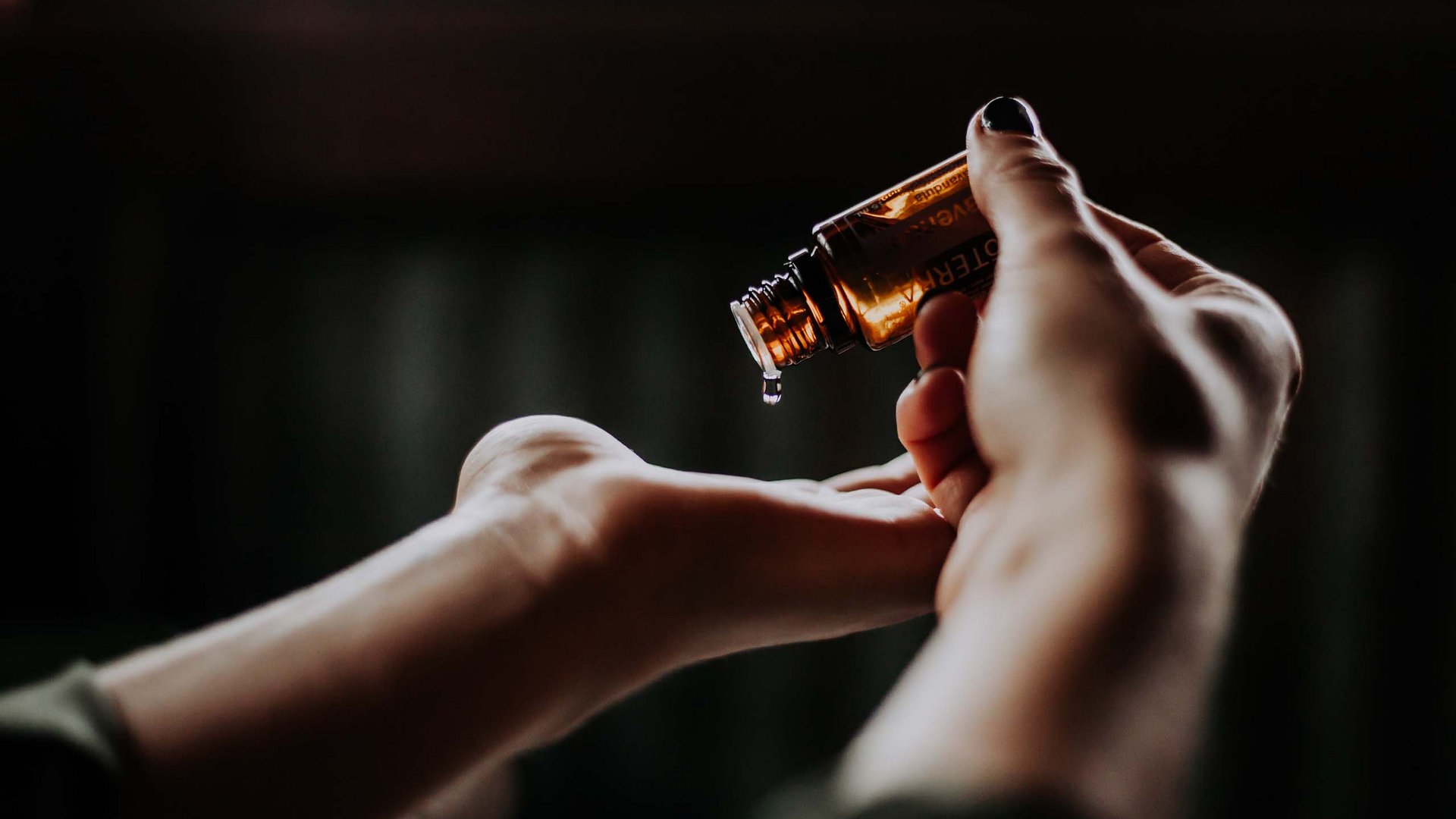 Hand dripping essential oil from brown bottle onto another hand